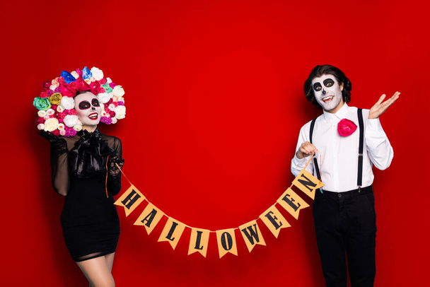 Photo of pretty spooky couple man lady hold flagged ribbon invite guest service theme event wear black short mini dress death costume roses headband suspenders isolated red color background. - Фото, зображення