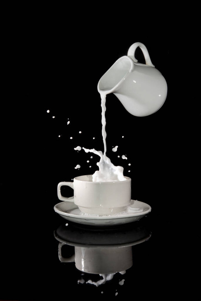 Pouring milk into the cup with splash all around on black - balance concept. - Foto, afbeelding