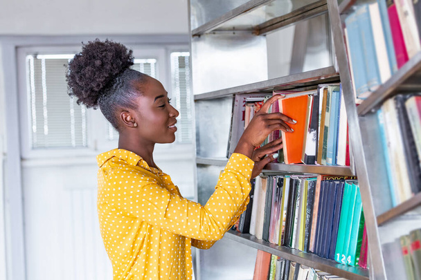 図書館の本棚から本を取っている女性。若い図書館員が図書館の書棚から本を探し、 1冊の本を取る - 写真・画像
