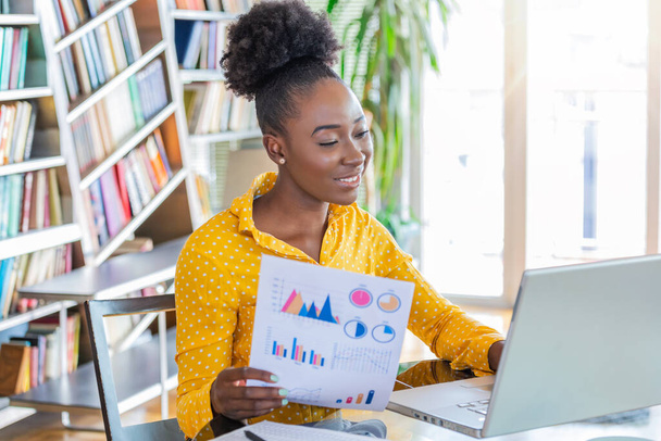Business professionals. Business woman analyzing data using computer while spending time in the office. Beautiful young grinning professional Black woman in office. Graphs and charts - Фото, зображення