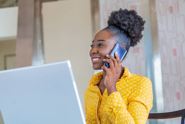 Успешная деловая женщина, работающая в офисе, афроамериканка, разговаривающая по мобильному телефону и работающая на ноутбуке. Концепция малого бизнеса - Фото, изображение