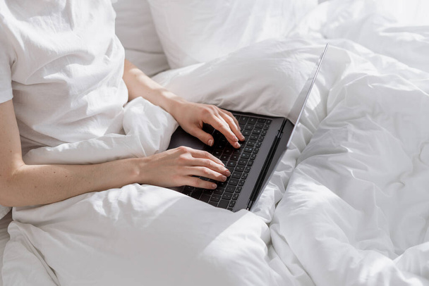 Przycięty widok freelancer blogger podróży pracy na jej nowoczesnym laptopie leżącego w łóżku. Kobieta korzystająca z komputera, dokonywania zakupów online lub surfingu w Internecie czytanie wiadomości, odpoczynek w wygodnej sypialni w pokoju hotelowym - Zdjęcie, obraz