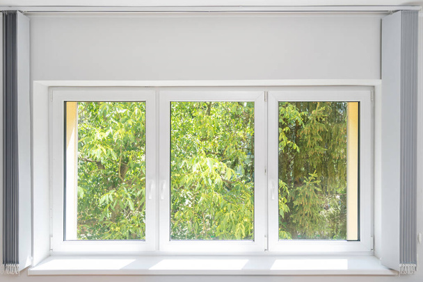 janela de pvc de plástico fechado com moldura branca instalada em casa, peitoril e tecido vertical aberto jalousie, vista sobre árvores verdes - Foto, Imagem