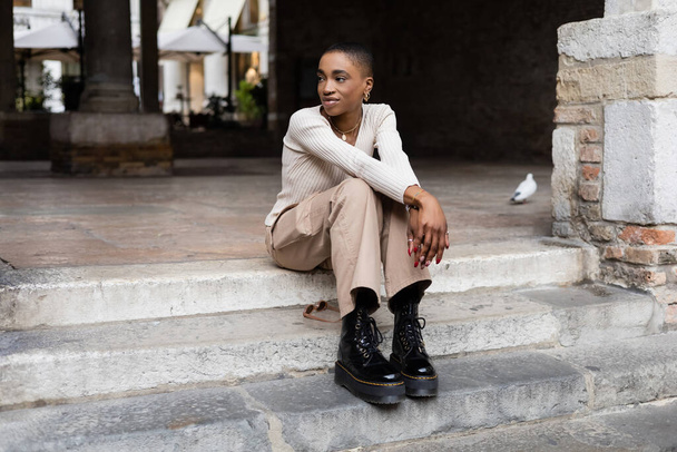 Fashionable african american woman sitting on stairs on city street in Italy - Foto, Bild