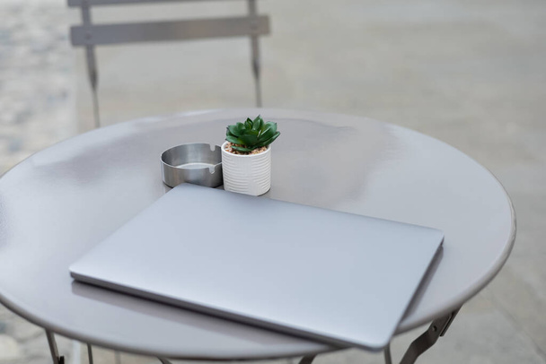 Φορητός υπολογιστής κοντά στο φυτό και τασάκι σε bistro τραπέζι σε εξωτερικούς χώρους  - Φωτογραφία, εικόνα