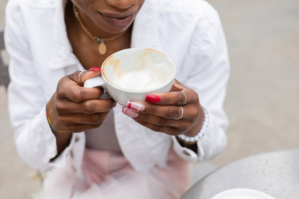 Cropped view of stylish african american woman holding cup of cappuccino outdoors   - Photo, Image