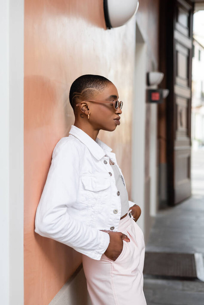 Side view of trendy african american woman in sunglasses posing near building on street in Treviso - Foto, Imagem