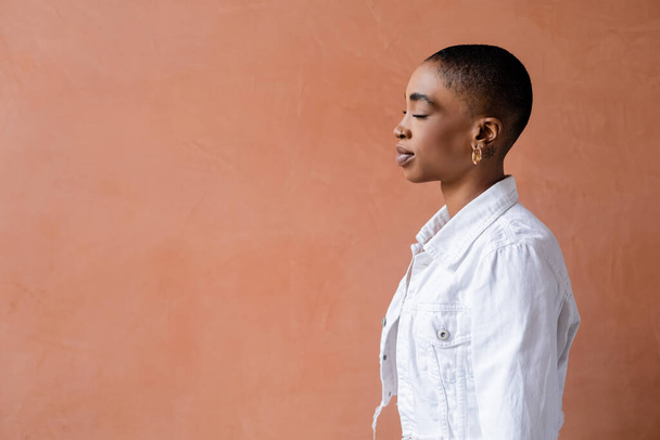 Vue latérale de la femme afro-américaine à la mode debout près du mur  - Photo, image