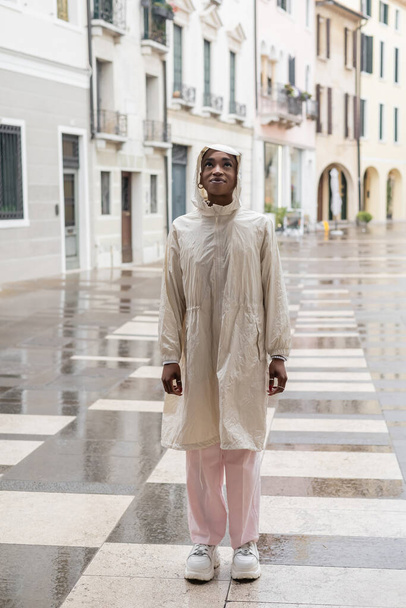 Modna afrykańska kobieta w płaszczu przeciwdeszczowym stojąca na zamglonej ulicy we Włoszech - Zdjęcie, obraz