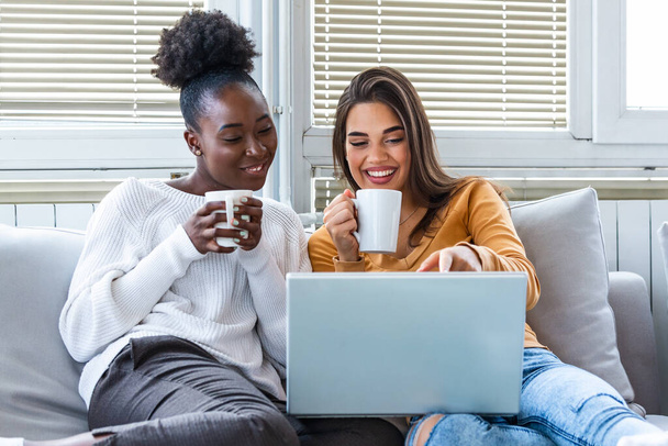 Portrait of funny and happy young women watching comedy or funny video in bed and laughing. Cheerful friends drinking coffee and looking movie with gladness. Cozy and friendly atmosphere - Foto, Bild