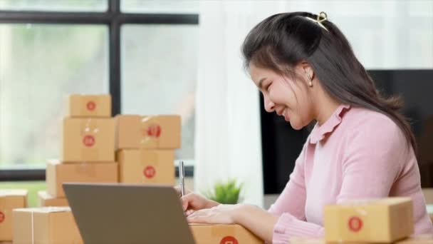 Woman who runs an e-commerce business is writing a list of customers on paper before shipping to them, she runs an e-commerce business on websites and social media. Concept of selling products online. - Metraje, vídeo