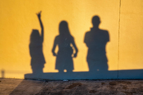 Σκιές μιας οικογένειας τριών ανθρώπων στον τοίχο την ώρα του ηλιοβασιλέματος. Ομάδα ανθρώπινων σκιών στο φόντο του πέτρινου τοίχου. - Φωτογραφία, εικόνα