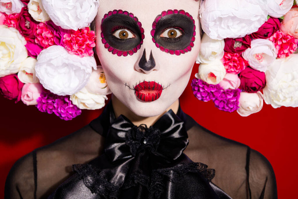 Closeup photo of voodoo awake dead witch religion folklore creepy creature, death day face print makeup holiday masquerade wear floral headwear band black costume isolated red background. - 写真・画像