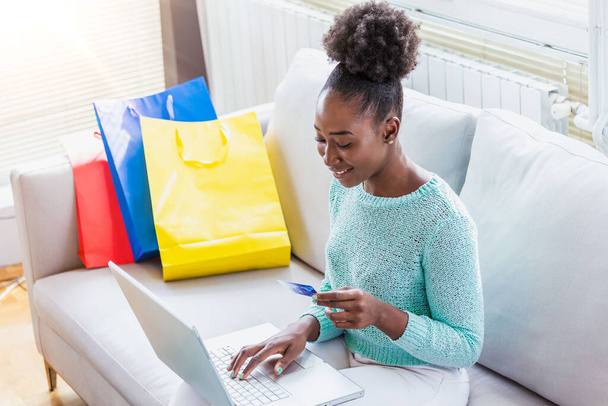 Γυναίκα κατέχει πιστωτική κάρτα και τη χρήση φορητού υπολογιστή. Διαδικτυακή ιδέα αγορών. Νεαρό κορίτσι της Αφρικής Αμερικής αγοράζει είδη μόδας με τη χρήση πιστωτικής κάρτας - Φωτογραφία, εικόνα