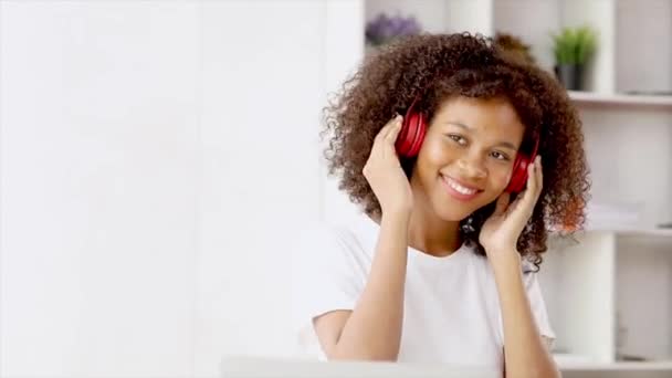 American woman wearing red headphones listening to music and dancing to soothing rhythms after a long online class, is a college student while studying online from home. Relaxing after class concept. - Footage, Video