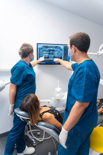 Clínica dental, paciente sentada hablando con los dentistas sobre sus dientes mirando la radiografía - Foto, imagen