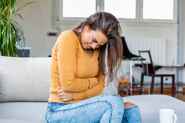 Young beautiful woman having painful stomachache. Woman with menstrual pain is holding her aching belly - body pain concept. woman having abdominal pain, upset stomach or menstrual cramps. - Фото, зображення