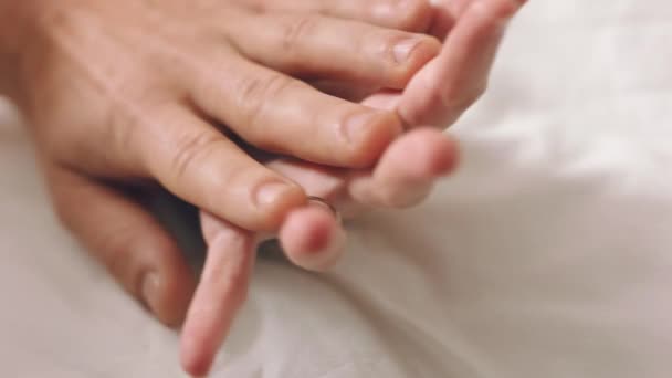 Couple, love and trust holding hands while in bed bonding, lying and touching with a wedding ring on wife sharing intimacy, support and commitment in marriage. Closeup of man and woman on honeymoon. - Footage, Video