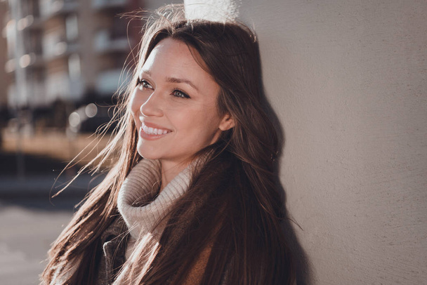 Fotografie krásné rozkošné ženy nosit šedý kabát usměvavý těší ranní slunce mimo městské ulice. - Fotografie, Obrázek