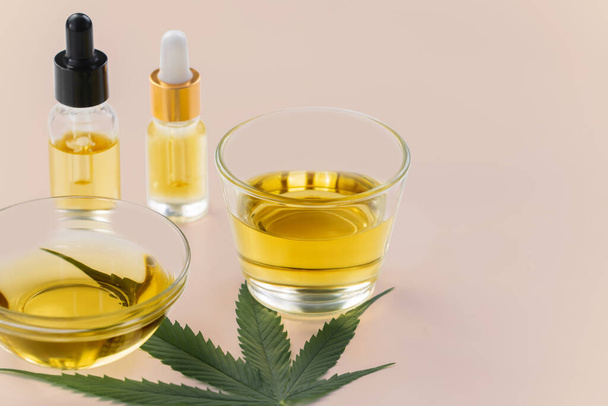 Glazen schaal en fles CBD olie, cannabis knop, en een hennepblad worden getoond van een witte achtergrond. Conceptie van gelegaliseerd olie-extract uit cannabis. - Foto, afbeelding