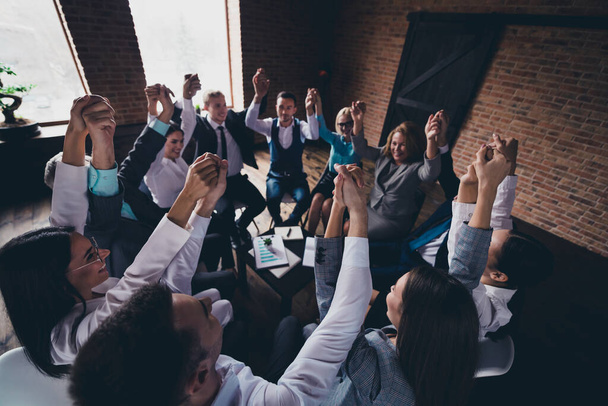 Portrait of delighted group business people sitting chair hold raise hands success achievement office indoors. - Foto, Imagem