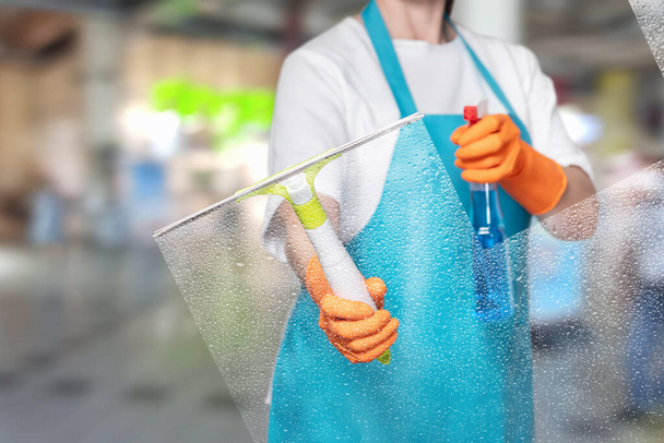 Ο καθαριστής σκουπίζει το γυαλί με ένα εργαλείο σε ένα θολό φόντο. - Φωτογραφία, εικόνα