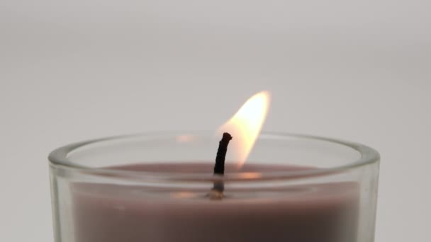 Round brown single Candle flickering on white background. Side view. Candle in glass candle holder burning on the light background. Slow motion full HD video - 映像、動画