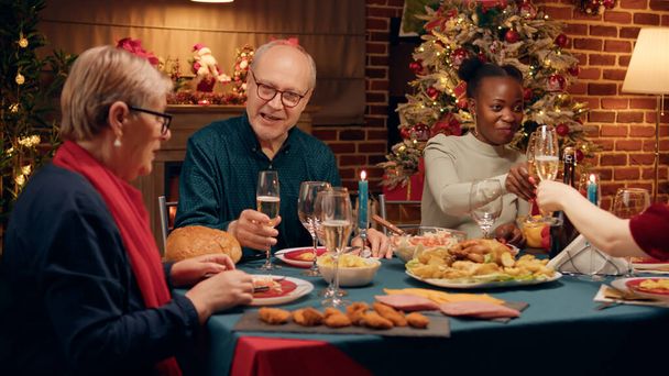 Szczęśliwy starzec rozmawiający z żoną przy świątecznym stole z bliskimi członkami rodziny. Wieloetniczni świąteczni ludzie świętują tradycyjne zimowe wakacje jedząc domowe jedzenie. - Zdjęcie, obraz