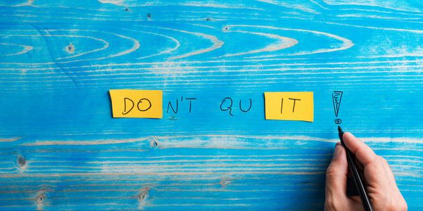 Male hand writing a Dont quit, Do it sign on bright yellow papers over aged blue wooden background. - Fotó, kép