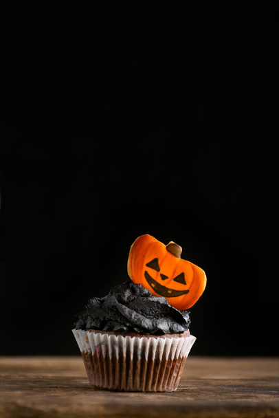 Heerlijke Halloween feest zwarte cupcake met peperkoek pompoenen op zwarte achtergrond. verticaal frame. Kopieerruimte - Foto, afbeelding