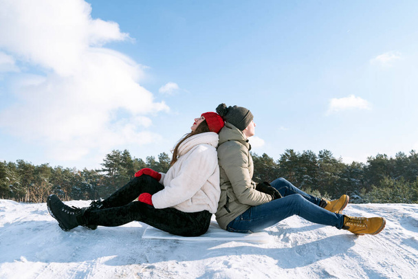 Guy and girl sit back to back in the snow. Active winter recreation. - Photo, Image