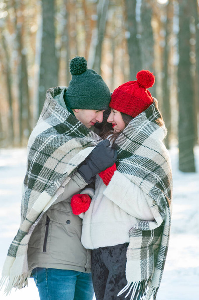 Mladý zamilovaný pár v zasněženém zimním parku se přikryl teplou přikrývkou. Svislý rámec. - Fotografie, Obrázek