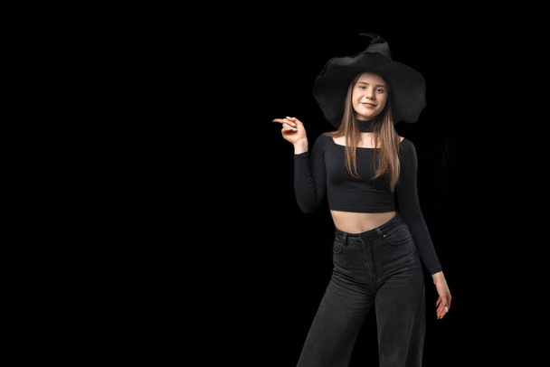 Młoda wiedźma w szpiczastym kapeluszu wskazuje palcem na puste czarne tło. Odbiór. Miejsce na tekst - Zdjęcie, obraz