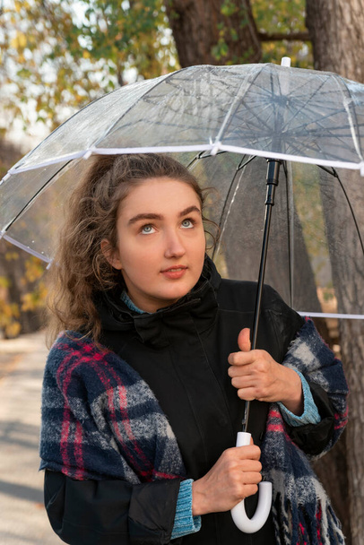 Portrait of young woman looking up from under transparent umbrella. Girl with blue eyes and brown hair. - Foto, afbeelding