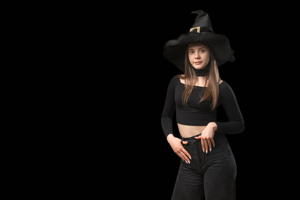 Młoda dziewczyna nosi czarny top i spiczasty kapelusz. Portret nastolatki na czarnym tle. Przestrzeń kopiowania - Zdjęcie, obraz