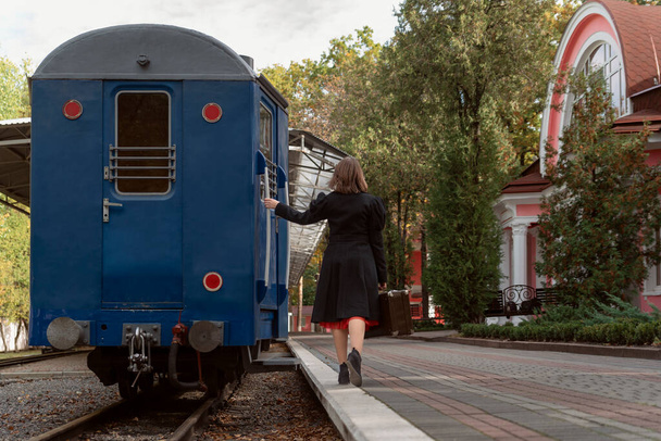 Woman with a suitcase in her hands hurries to board the departing train. Train station, rear view. - Foto, afbeelding