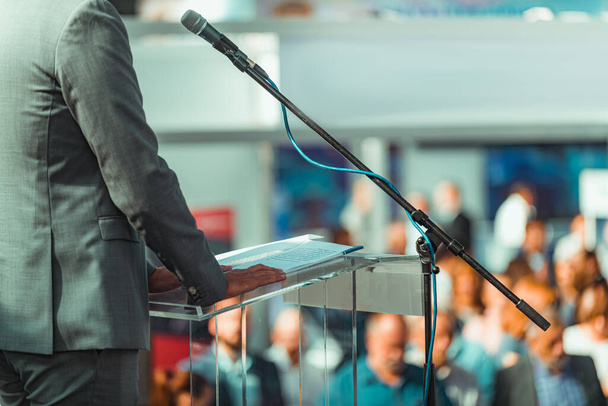 Мужчина в костюме спикера, стоящий перед микрофонами на пресс-конференции
. - Фото, изображение