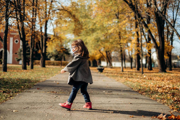 Happy cute girl in a fashionable coat and stylish glasses walks and laughs, the child enjoys time in a warm autumn park, a happy childhood - Fotó, kép