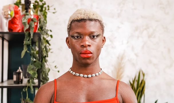Afroamerykańska transseksualistka z farbowanymi włosami i stylowym makijażem patrząca na kamerę w dzień w domu - Zdjęcie, obraz