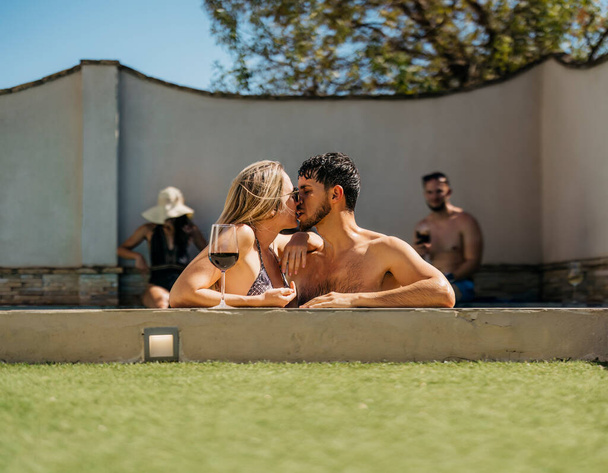 Caucasian couple kissing leaning on the edge of a swimming pool. Holidays - Photo, Image