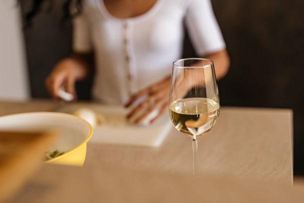 a womans glass of white wine while preparing a salad in the kitchen - Photo, Image