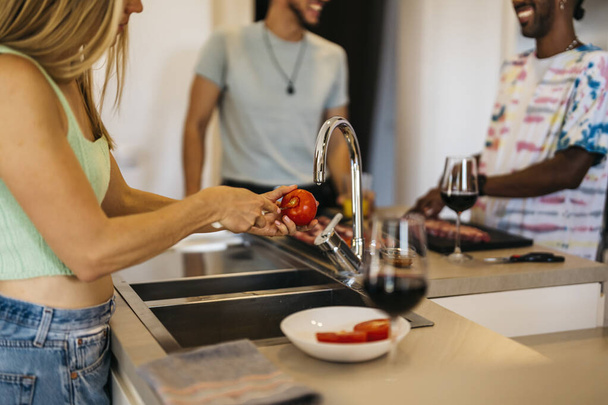 Egy szőke nő meghámozza a paradicsomot a barátok társaságában a konyhában. - Fotó, kép