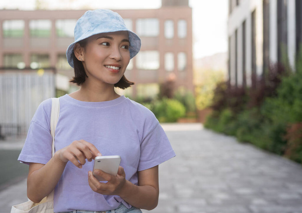 Uśmiechnięta stylowa azjatycka kobieta korzystająca z telefonu komórkowego zakupy online na ulicy, przestrzeń do kopiowania. Bankowość mobilna  - Zdjęcie, obraz