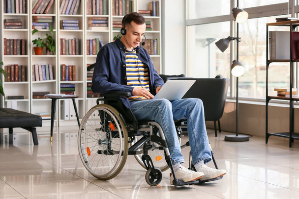Young man in wheelchair using laptop at home - 写真・画像
