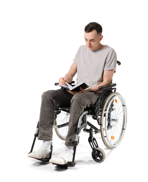 Młody człowiek na wózku inwalidzkim czyta książkę odizolowany na białym - Zdjęcie, obraz