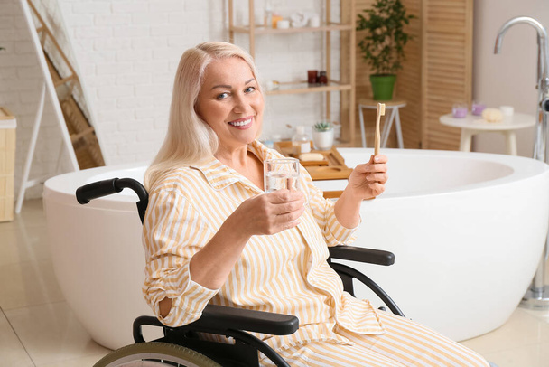 Зрелая женщина с ограниченными физическими возможностями чистит зубы в ванной комнате - Фото, изображение