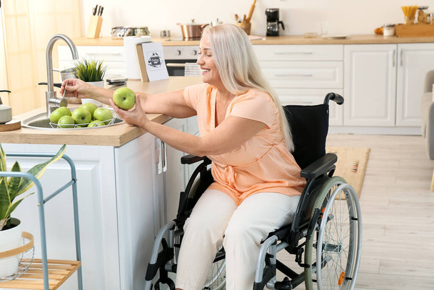 Femme mûre avec handicap physique laver les pommes dans la cuisine - Photo, image
