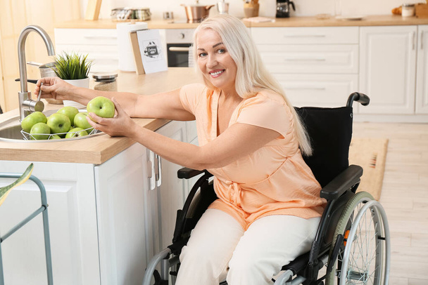 身体障害のある熟女台所でリンゴを洗う - 写真・画像