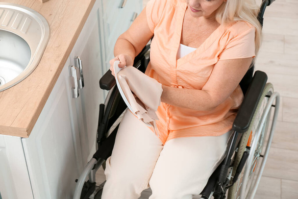 Mature woman with physical disability wiping dishes in kitchen - Photo, Image