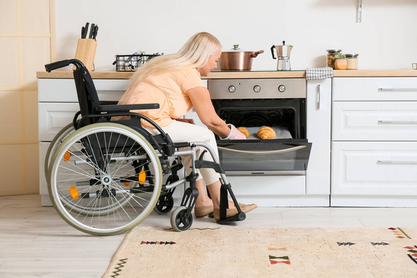 Fiziksel engelli olgun bir kadın mutfakta hamur işi pişiriyor. - Fotoğraf, Görsel